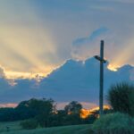 big wooden cross on green grass field under the white clouds